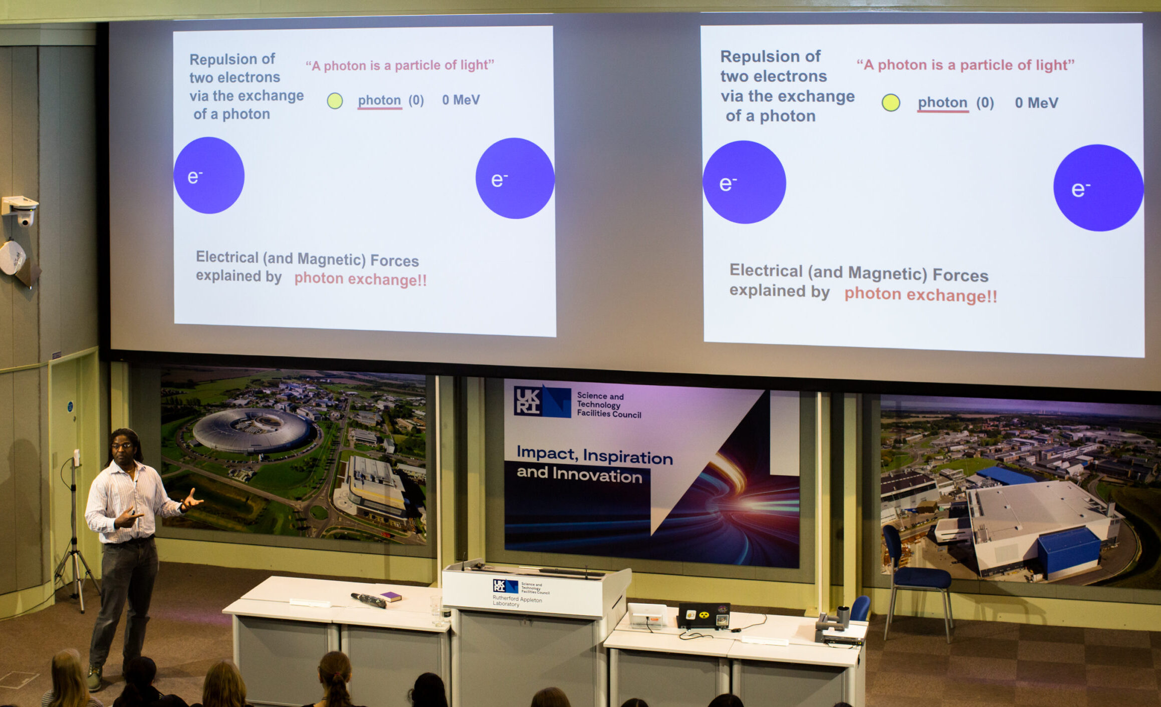 A member of staff is giving a talk to students in front of two screens showing a presentation slide about photons.