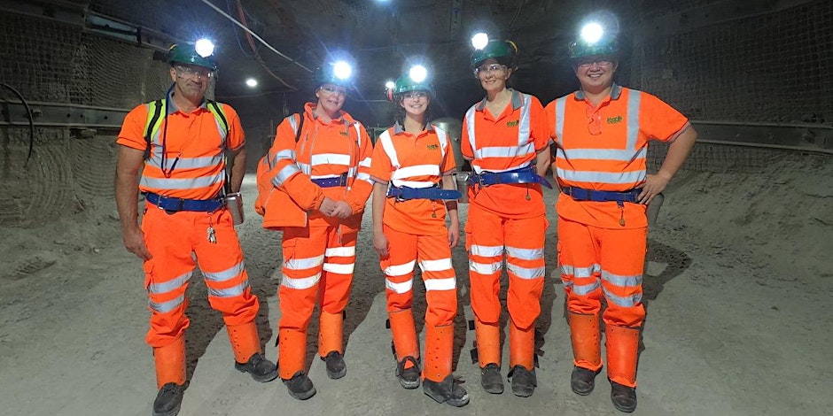 5 members of the Boulby team in their bright orange safety clothing standing in one of the mine tunnels